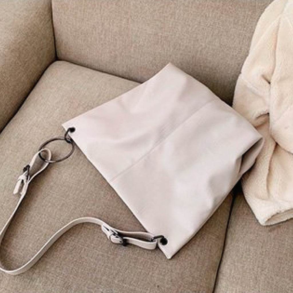 Ivory shoulder bag with ring strap hardware and fold-over slouchy body on couch