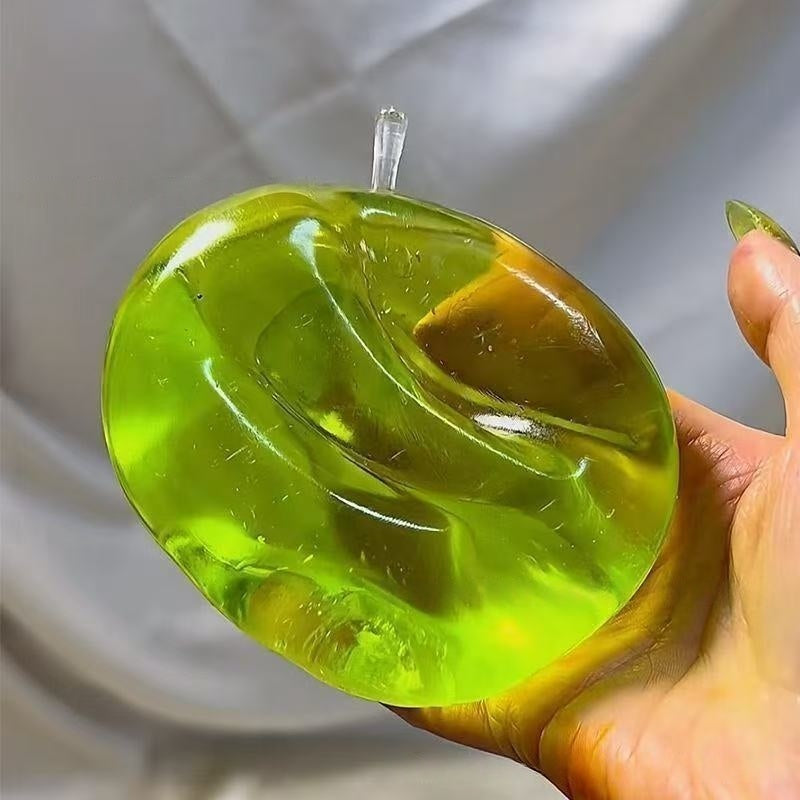Green translucent apple stress squeeze toy, creased surface from squeezing, stem visible