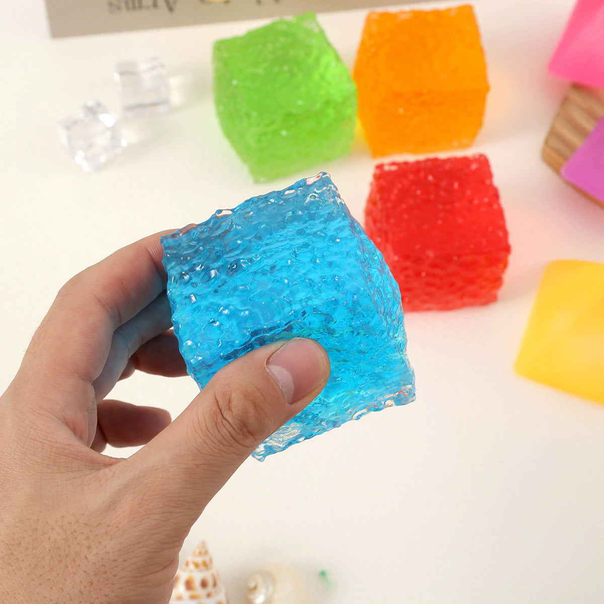 Hand holding a blue translucent squishy cube toy with bubble texture.