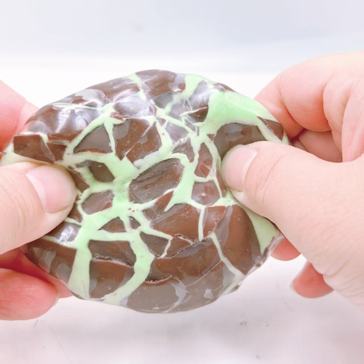 Chocolate brown and mint web-pattern crispy sphere stress-relief squeeze toy, held