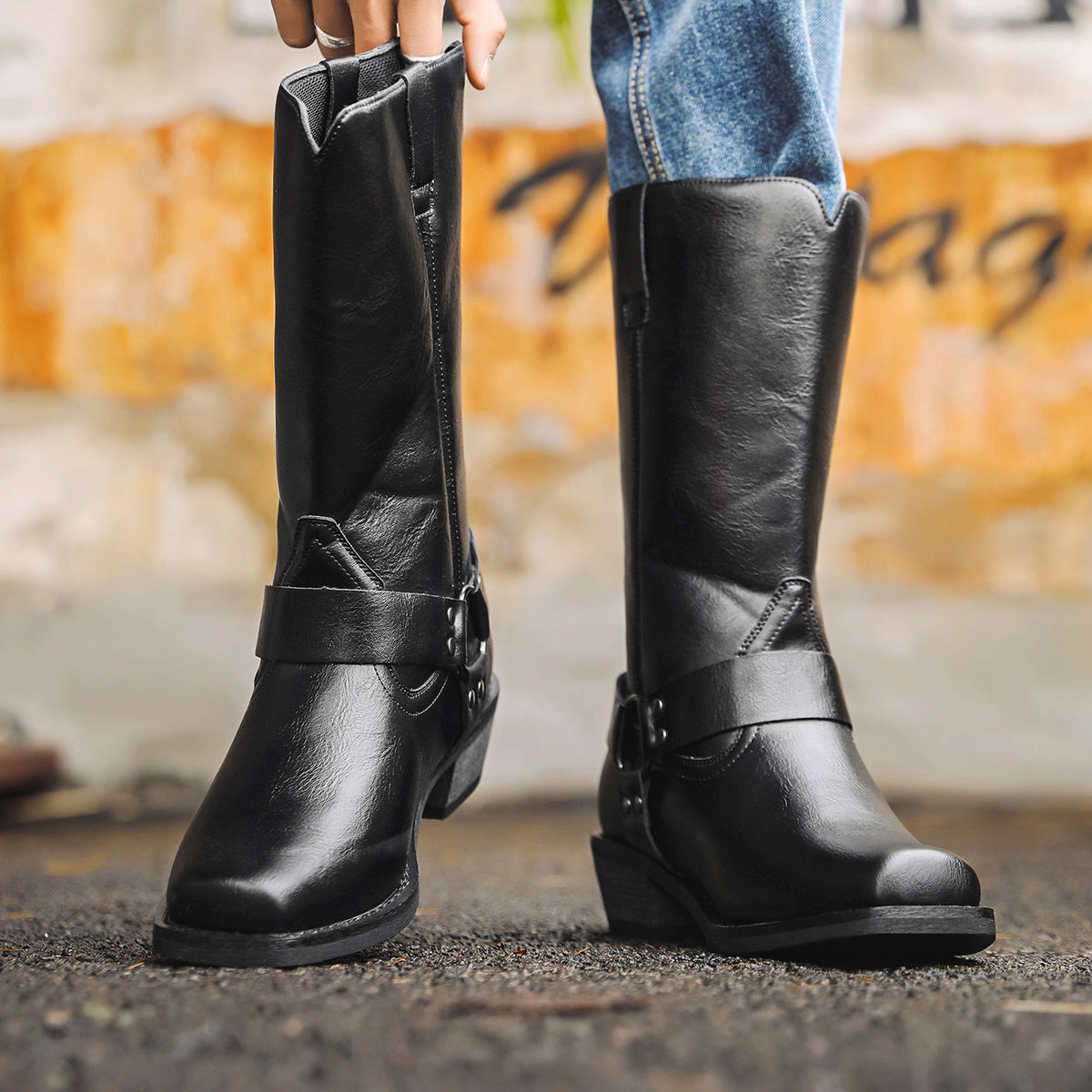 Black western cowboy boots with square toe and chunky heel, slip-on design with strap.