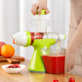 Green juicer machine with white hopper, squeezing fruit into a glass of red juice
