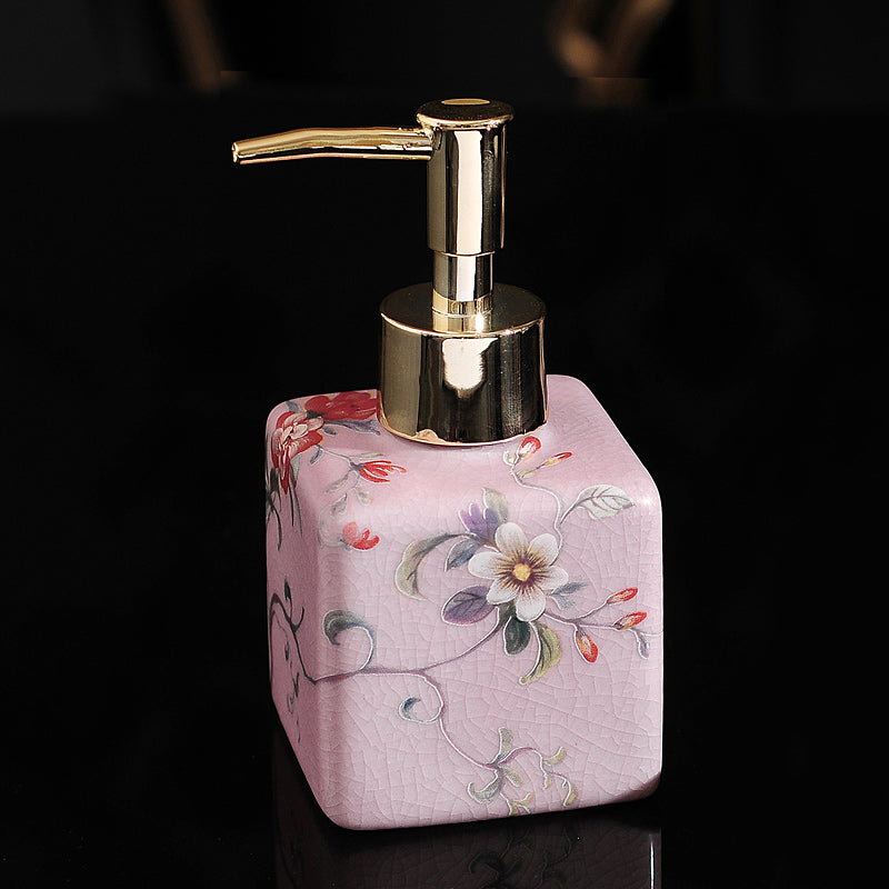 Hand-painted ceramic dispenser bottle, pink with purple floral detail, gold pump, rounded hexagon