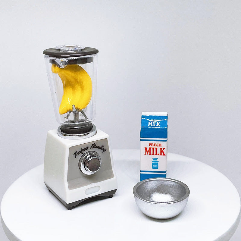 White toy blender with clear jar and black lid holding a yellow banana piece; milk bowl