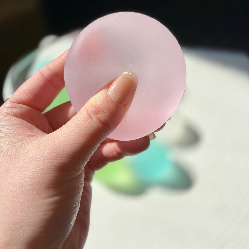 Translucent round squishy candy squeeze toy, pink, pressed between fingers