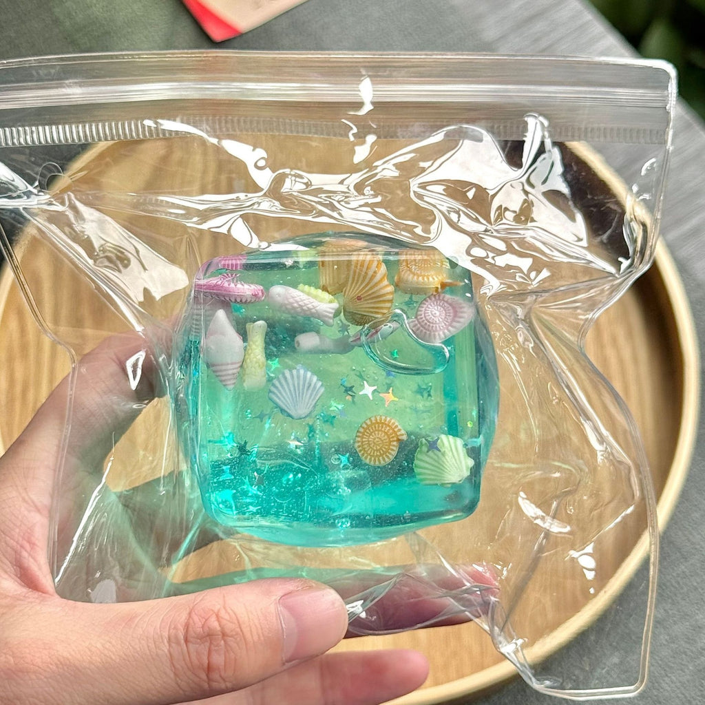 Translucent aqua blue squeeze cube toy in clear plastic, seashell and star icons