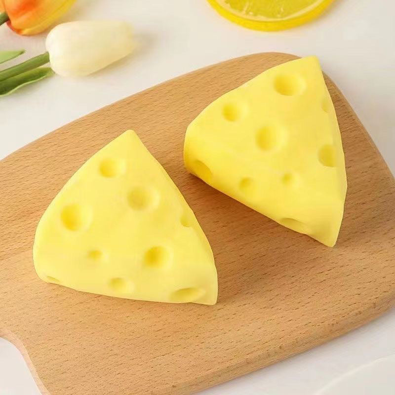 Yellow cheese wedge squishy toy with round holes, two pieces on a wooden board