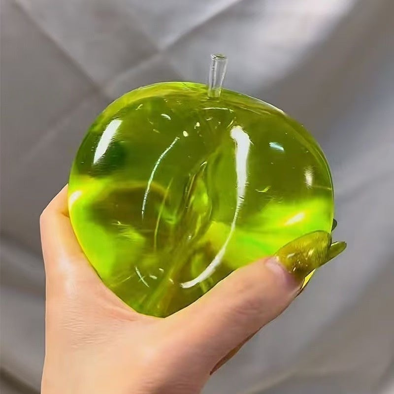 Green translucent apple stress squeeze toy, stem and side bump visible, held in hand