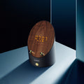 Grey speaker with wood top panel, glowing clock digits, and brass control buttons