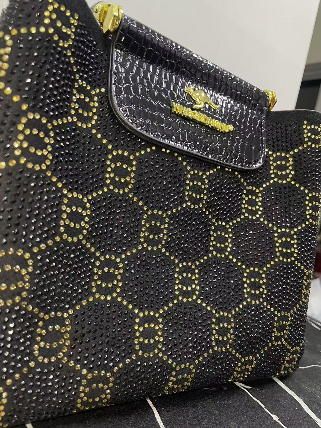 Close-up of black bag front with gold studded pattern and embossed front flap pocket
