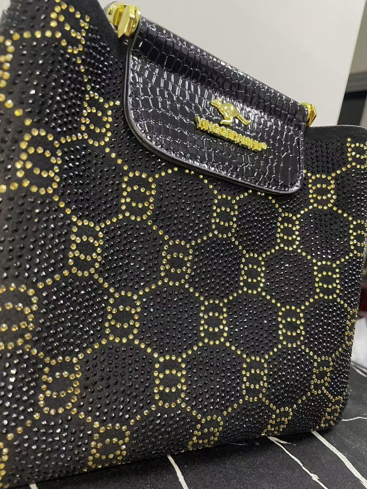 Close-up of black bag front with gold studded pattern and embossed front flap pocket