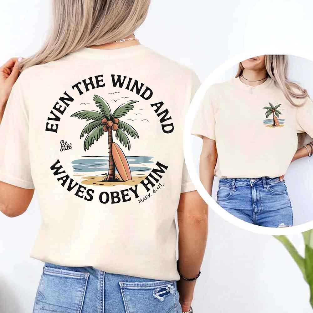 Light unisex tee with large back verse text "Even the Wind" and palm tree illustration