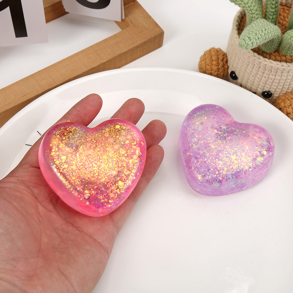 Pink and purple glitter heart squeeze stress toys in a hand