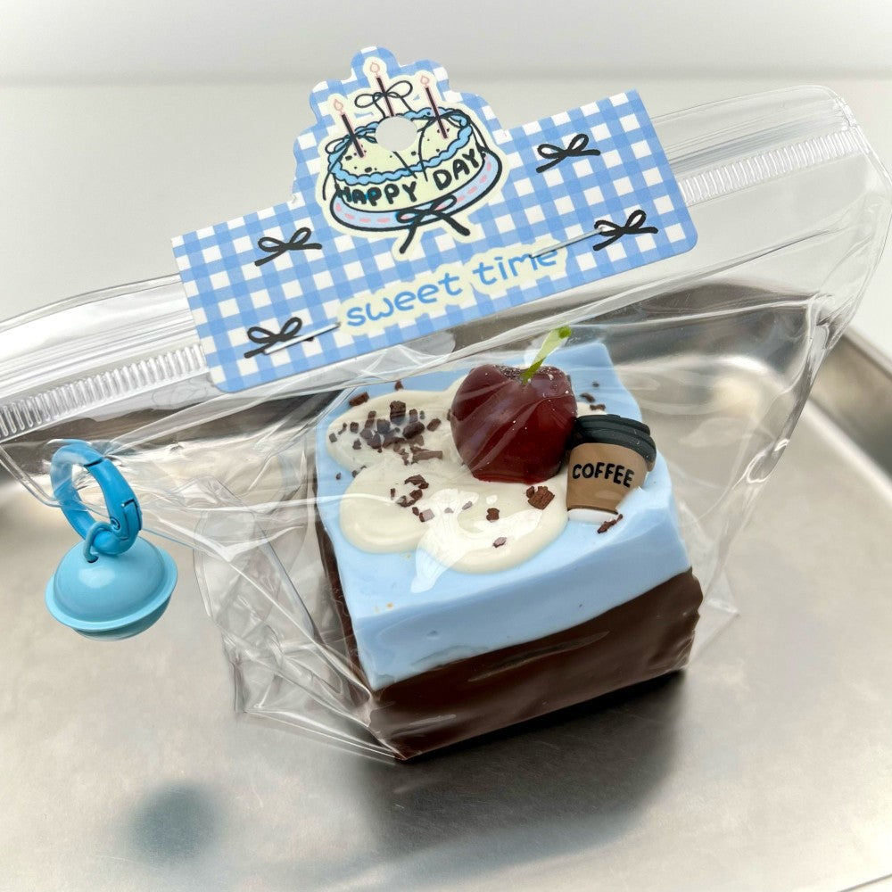 Cake-slice stress-relief clay gadget in clear bag, blue seal clip, blue and brown layers