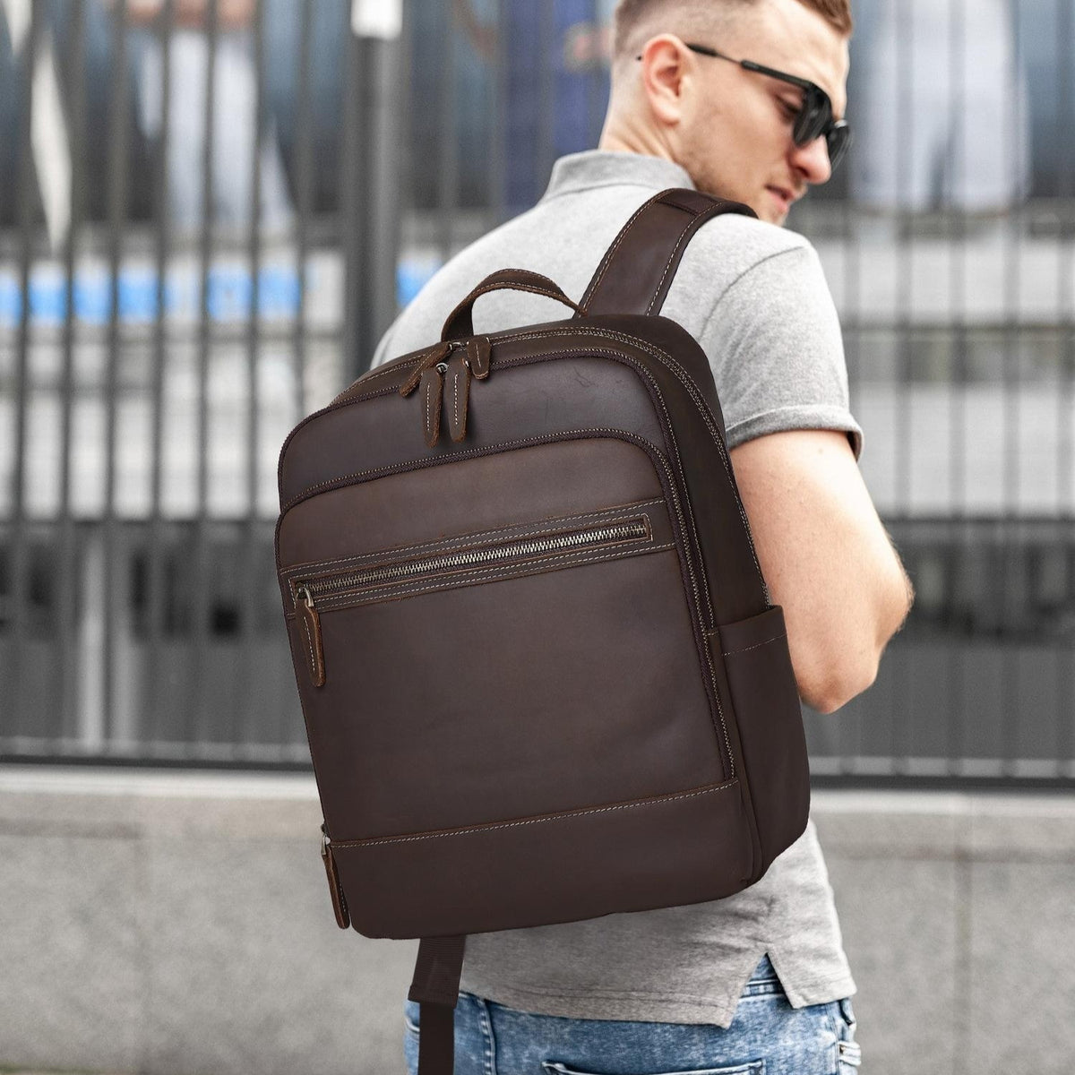 Coffee-brown leather backpack with top handle, front zip pocket, and adjustable shoulder strap