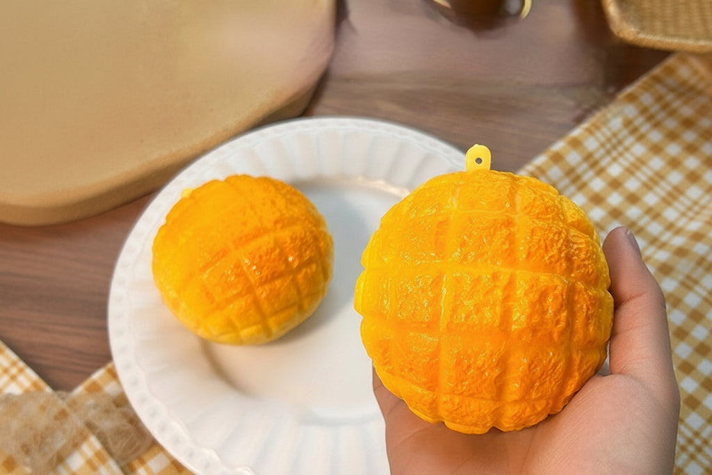 Orange pineapple bun stress ball squishy with small loop on top, on plate