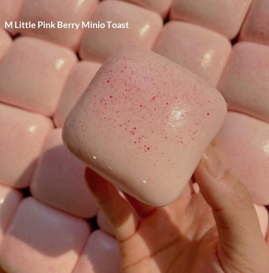Pink mini toast squishy squeeze toy with red speckles, held over pastel pile