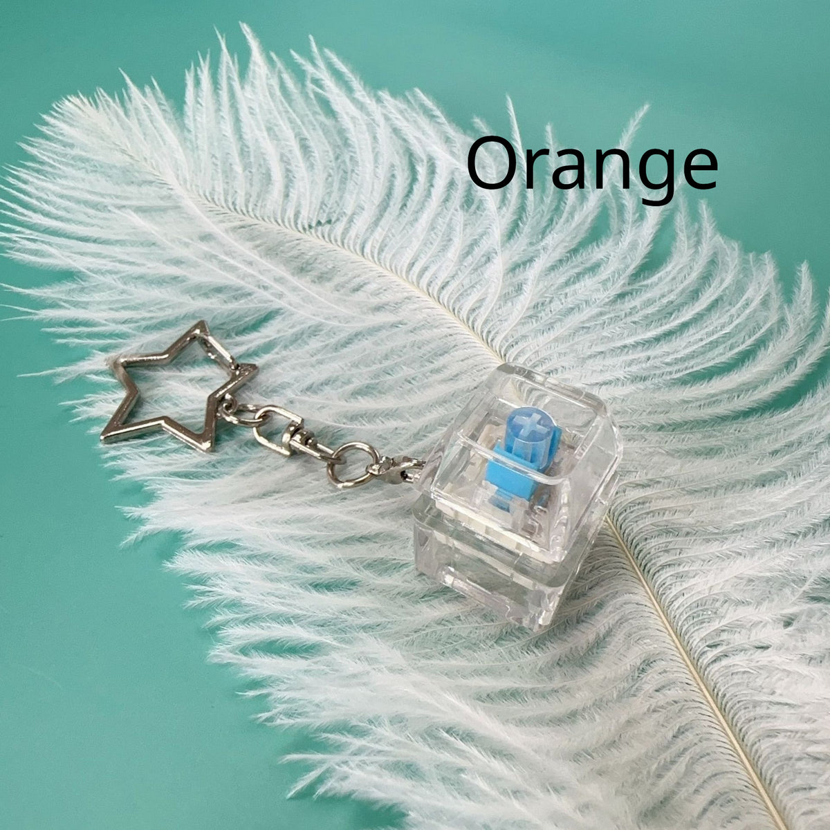 Orange mechanical key stress-relief toy with clear press piece, blue switch, star charm