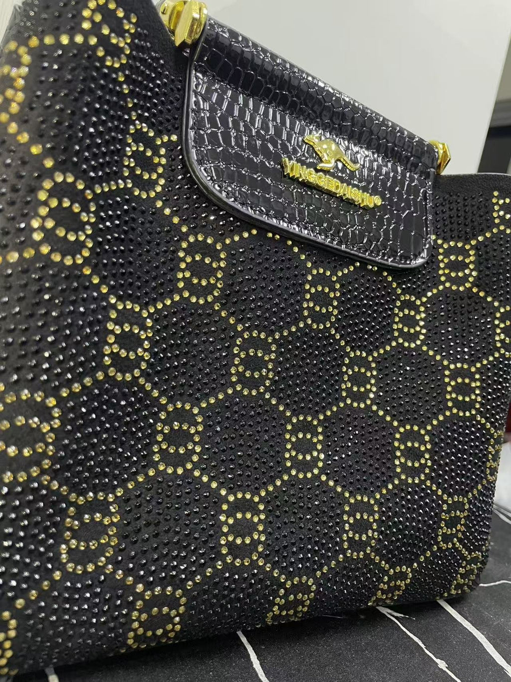 Close-up of black studded patterned bag with front flap pocket and gold hardware