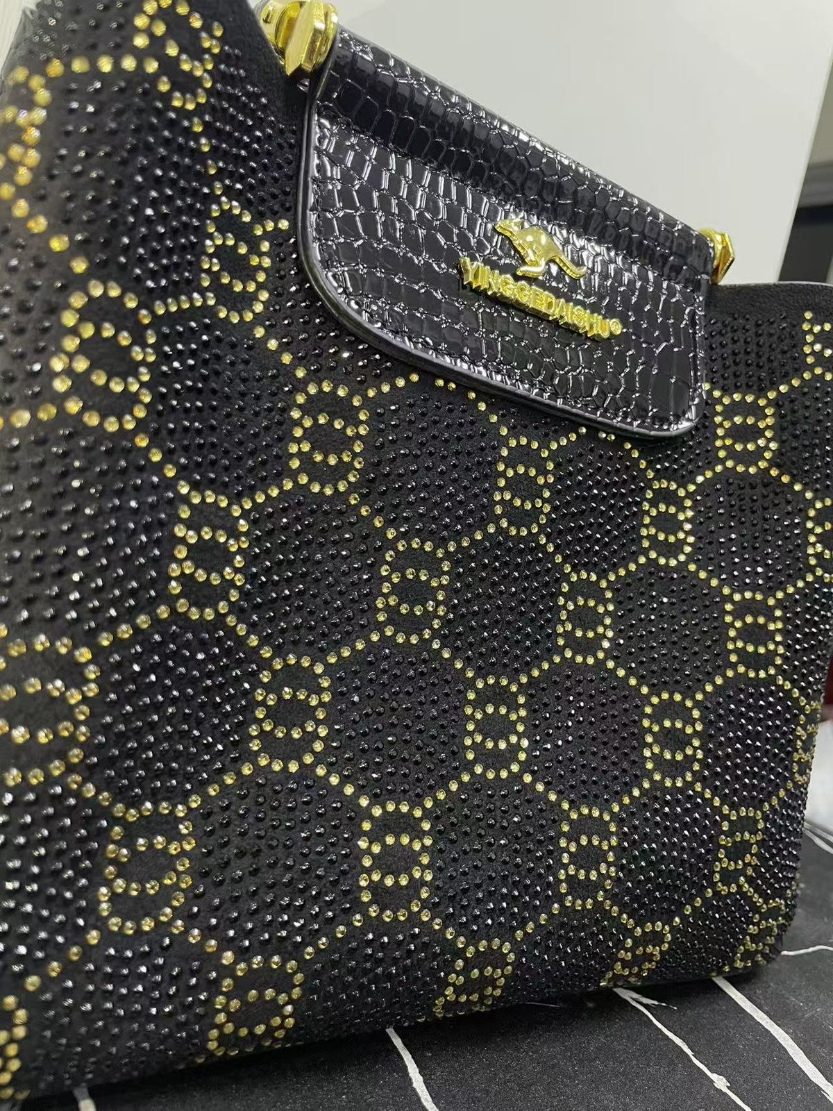 Close-up of black studded patterned bag with front flap pocket and gold hardware