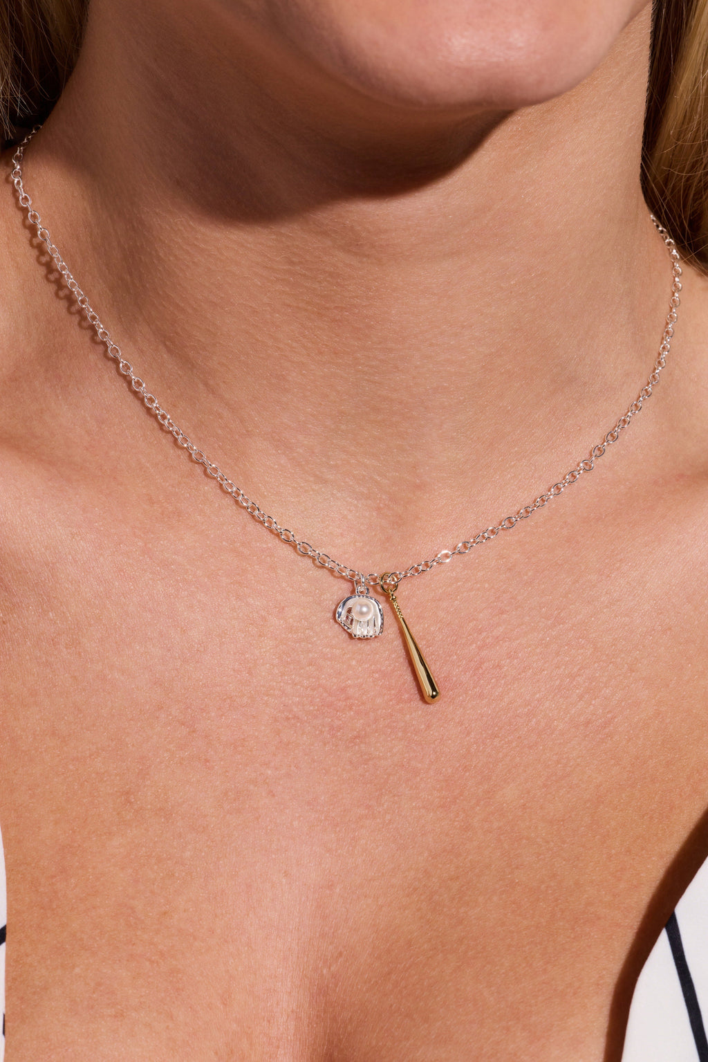 Two-tone pendant necklace on neck: silver chain with helmet and gold bat charms