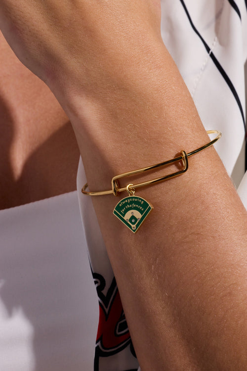 Gold charm bangle on wrist with green baseball diamond enamel charm