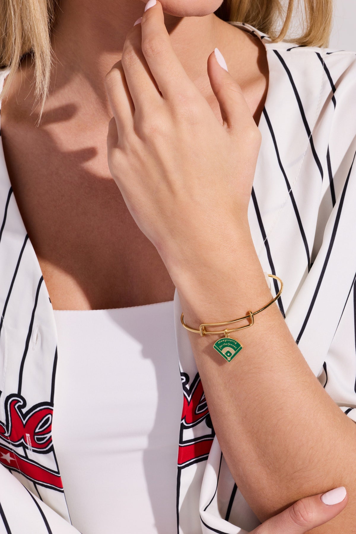 Gold charm bangle on wrist with green baseball diamond charm