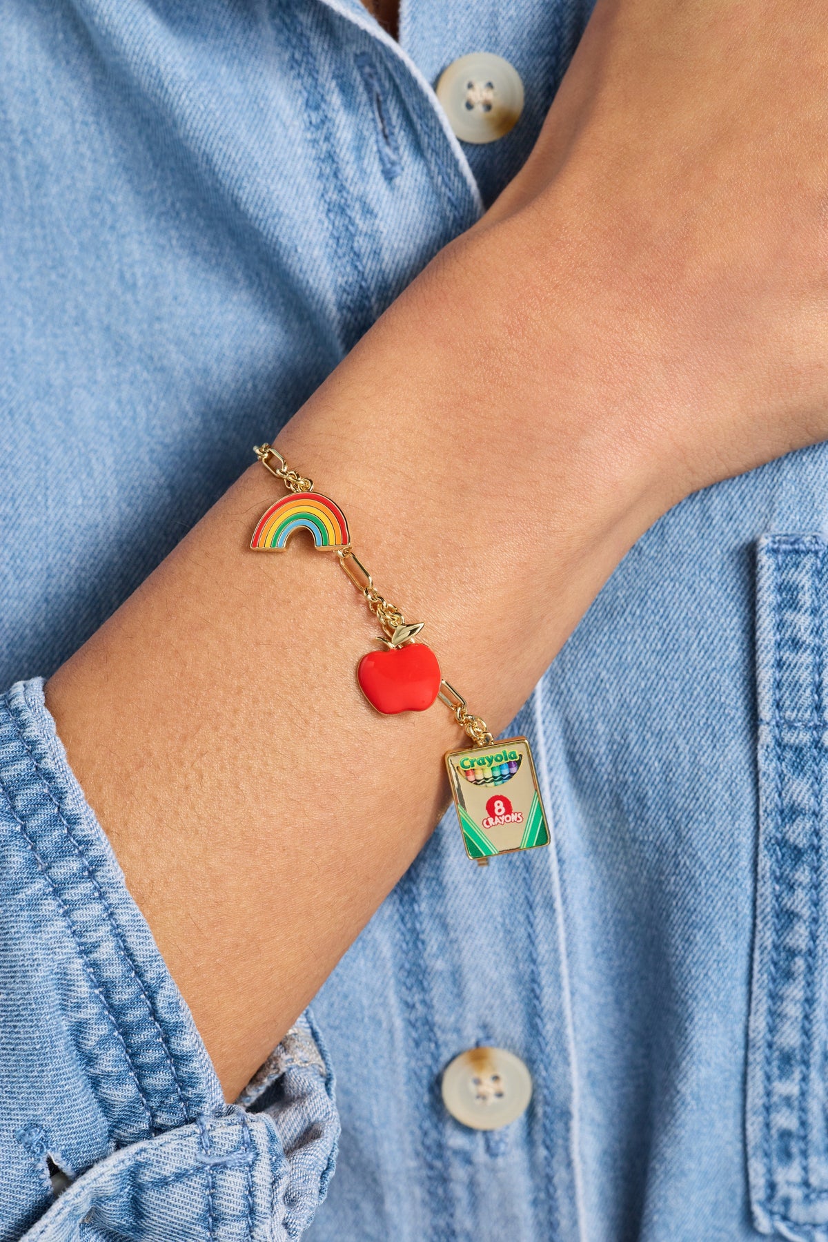 Gold toggle bracelet on wrist with rainbow charm, red apple heart, and crayon pack