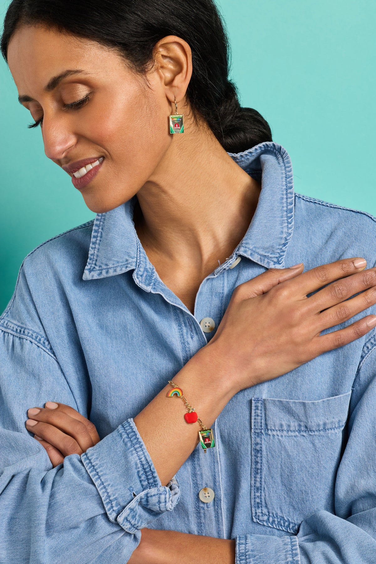 Gold bracelet with small rainbow charm and crayon-pack charm on wrist
