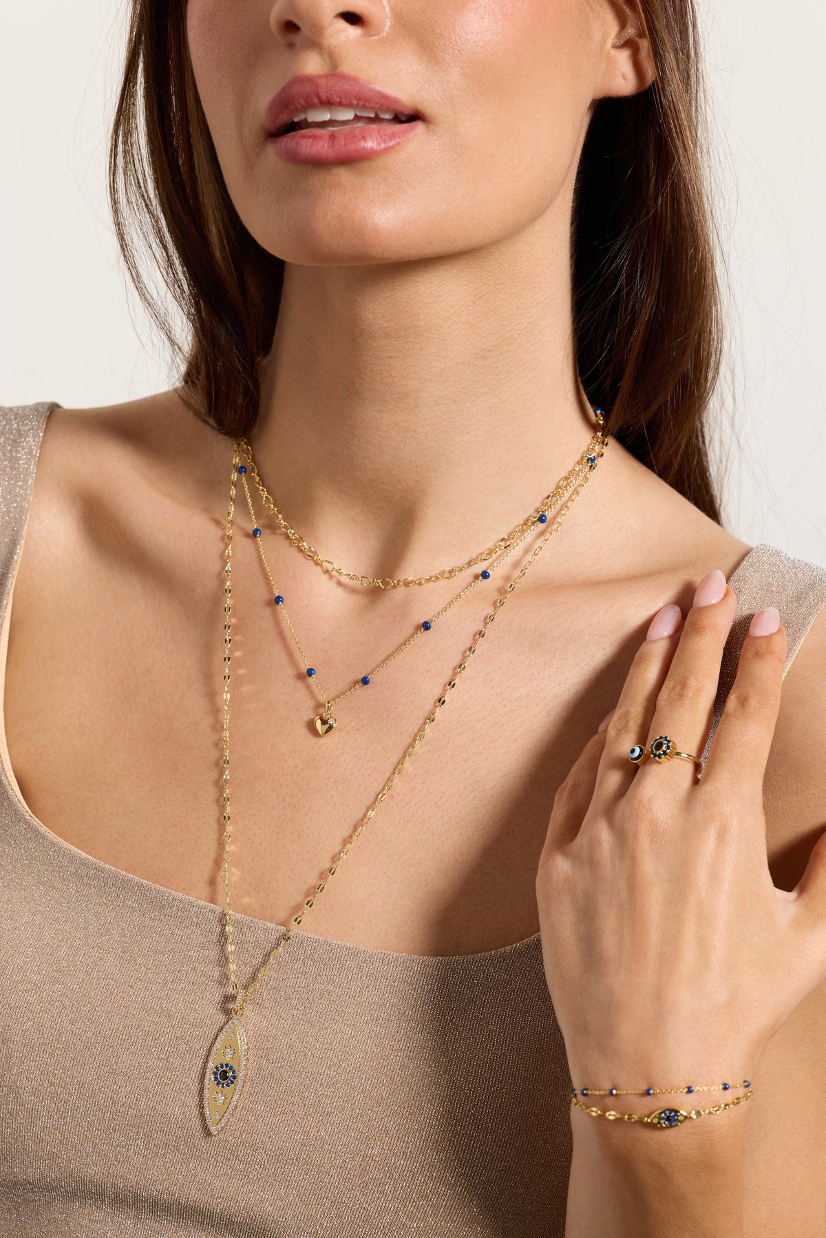 Gold evil eye pendant necklace with layered chains and blue bead details on model