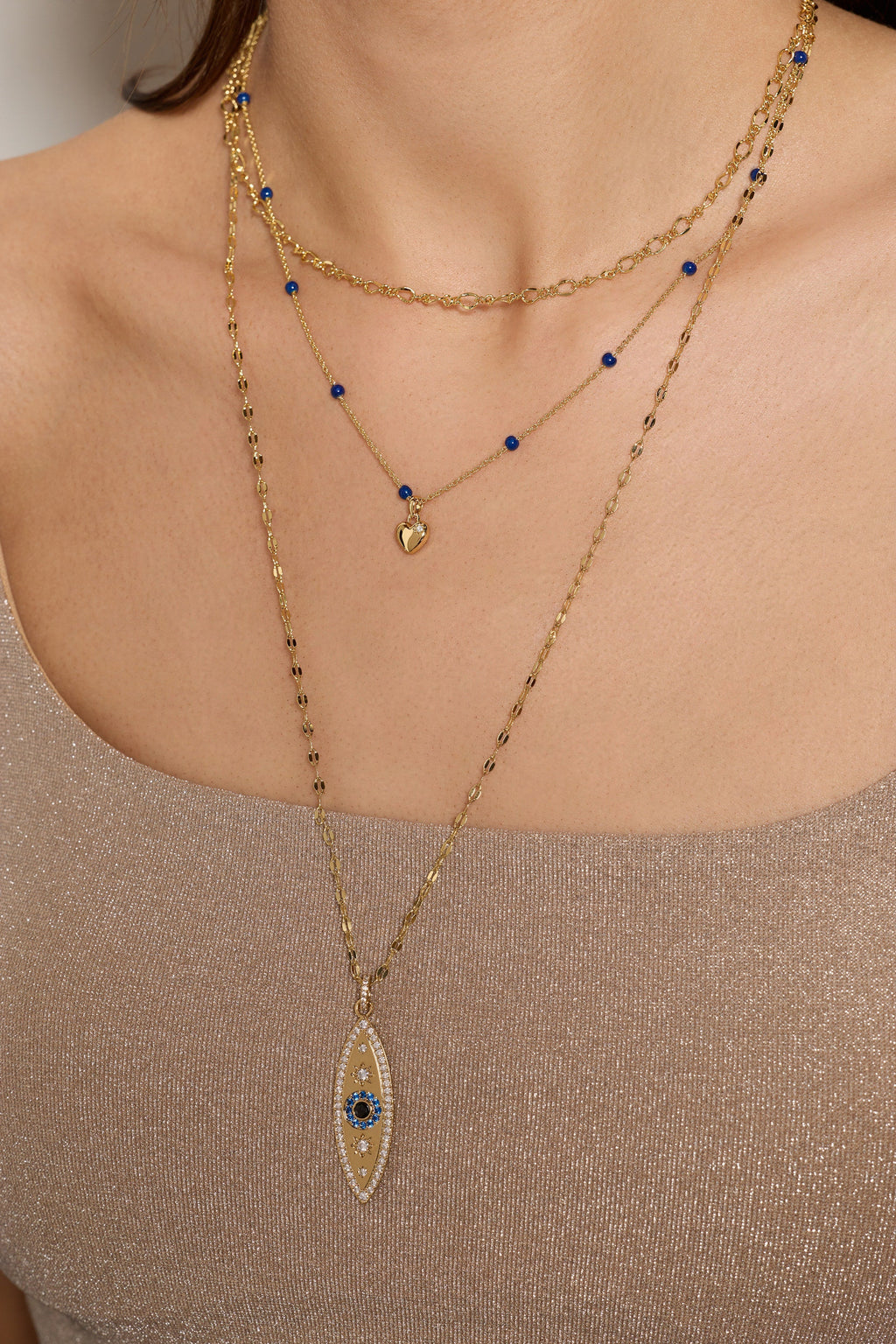 Gold evil eye necklace on neckline with multiple layers and small blue bead charms
