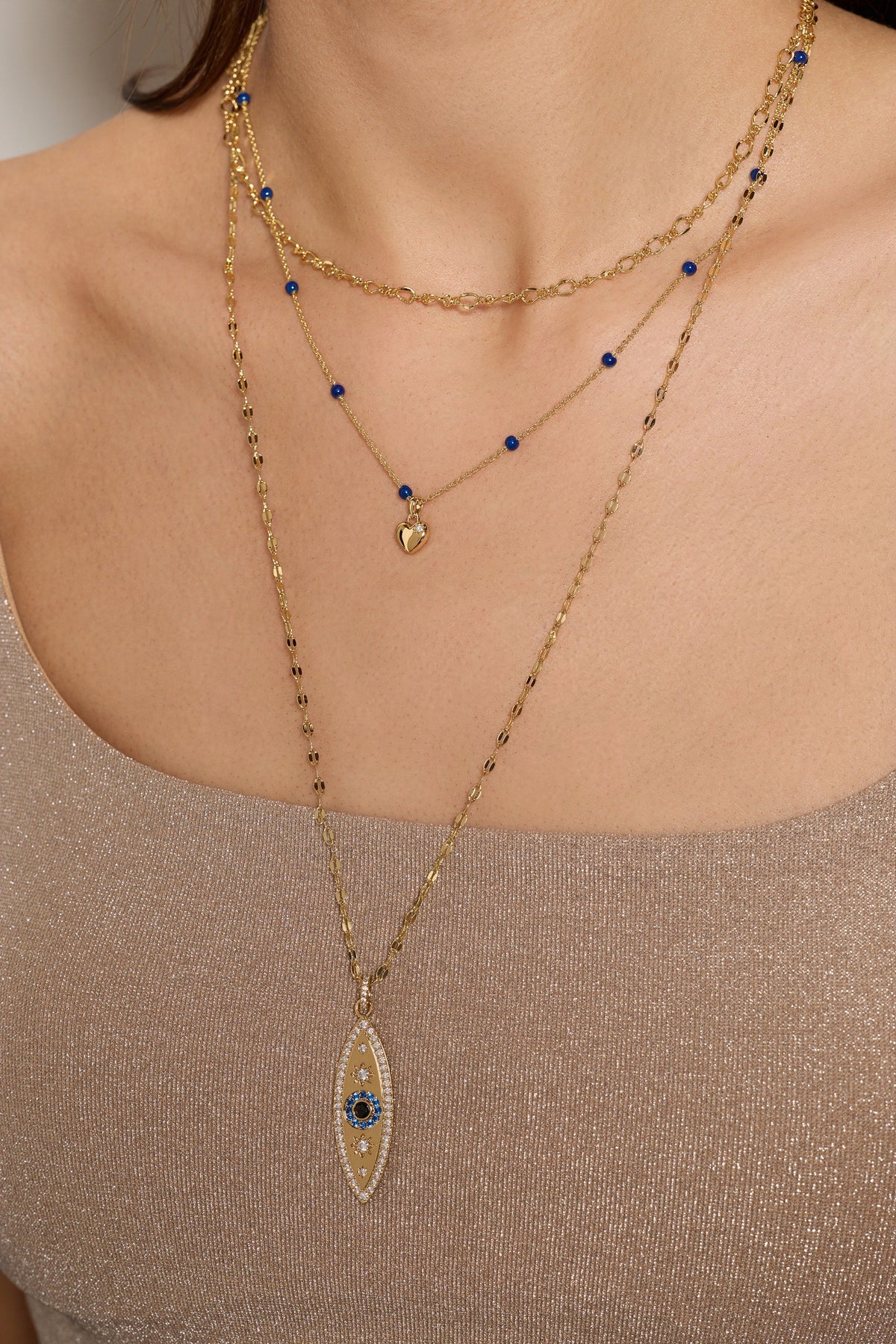 Gold evil eye necklace on neckline with multiple layers and small blue bead charms