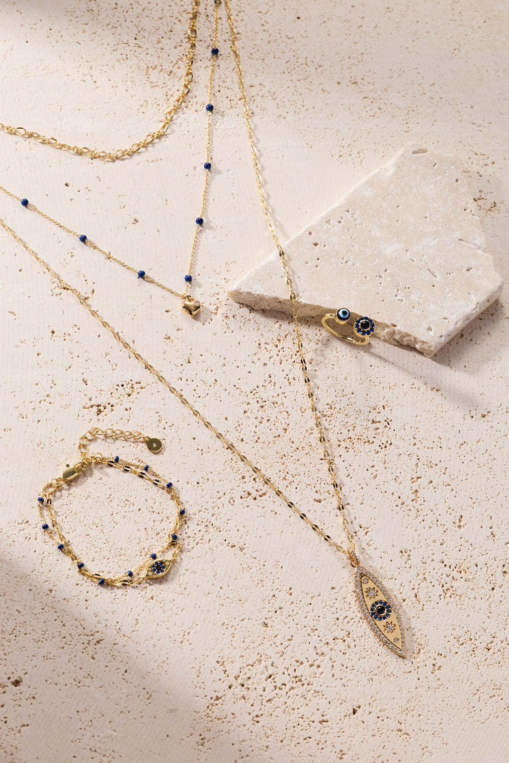 Gold layered evil eye charm necklaces with blue enamel beads on a light surface
