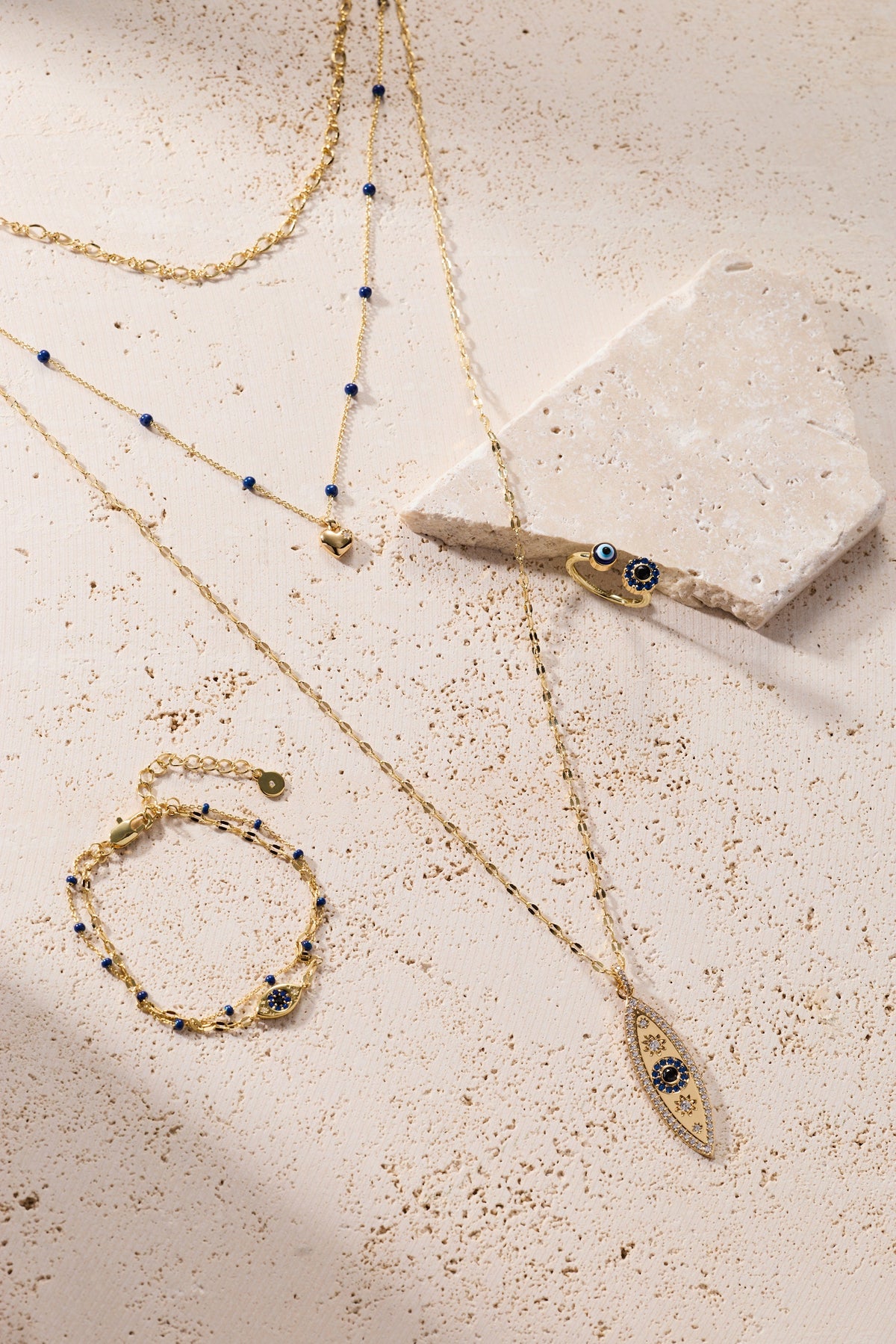 Gold layered evil eye charm necklaces with blue enamel beads on a light surface