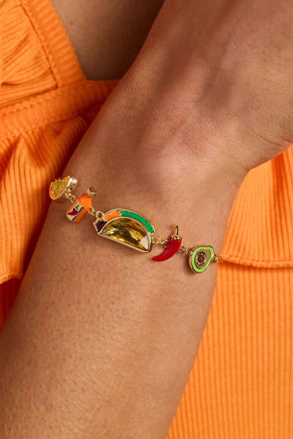 Gold-tone taco charm bracelet on wrist with red chili and green citrus charms