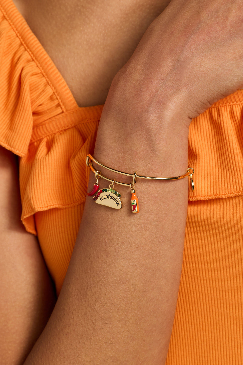 Gold multi-charm bangle on wrist with taco and chili charms