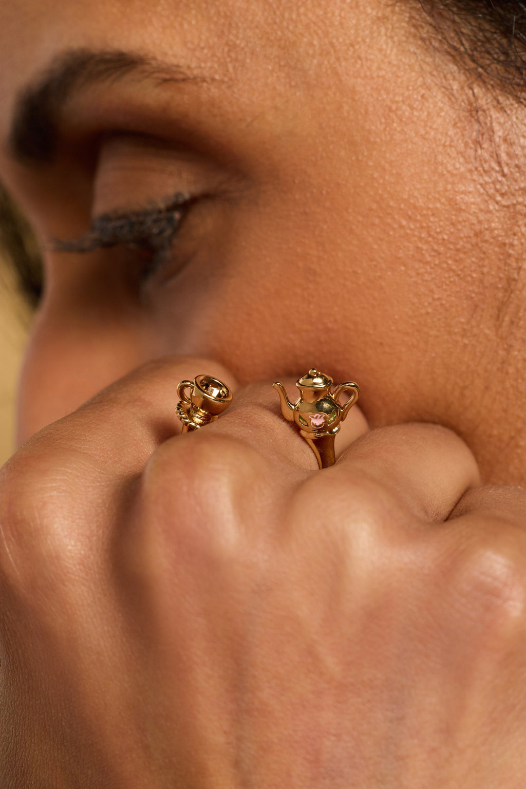 Gold-tone charm ring with teapot and cup details and gemstone accents on finger