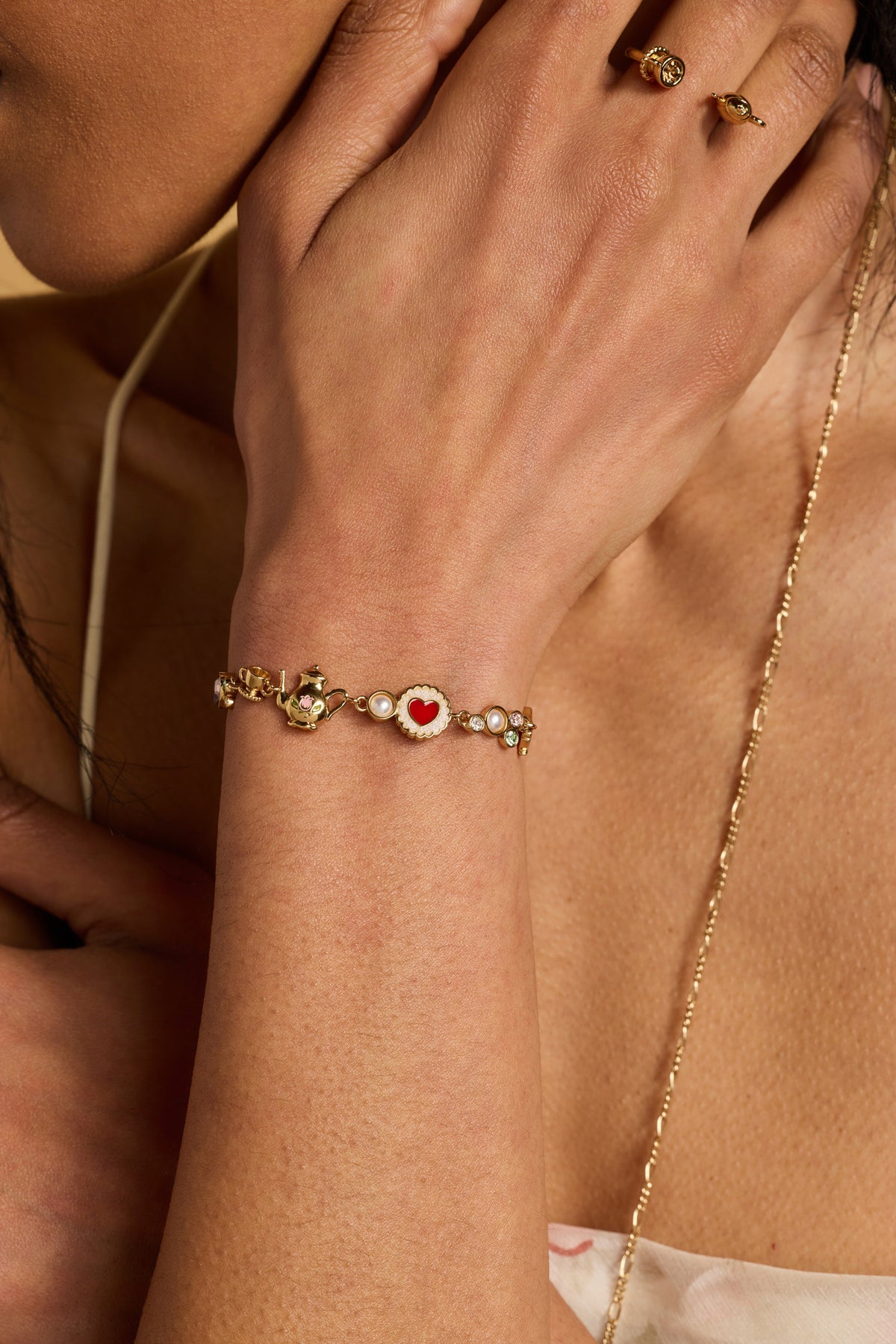 Gold-tone bolo bracelet on wrist with heart and pearl charm accents
