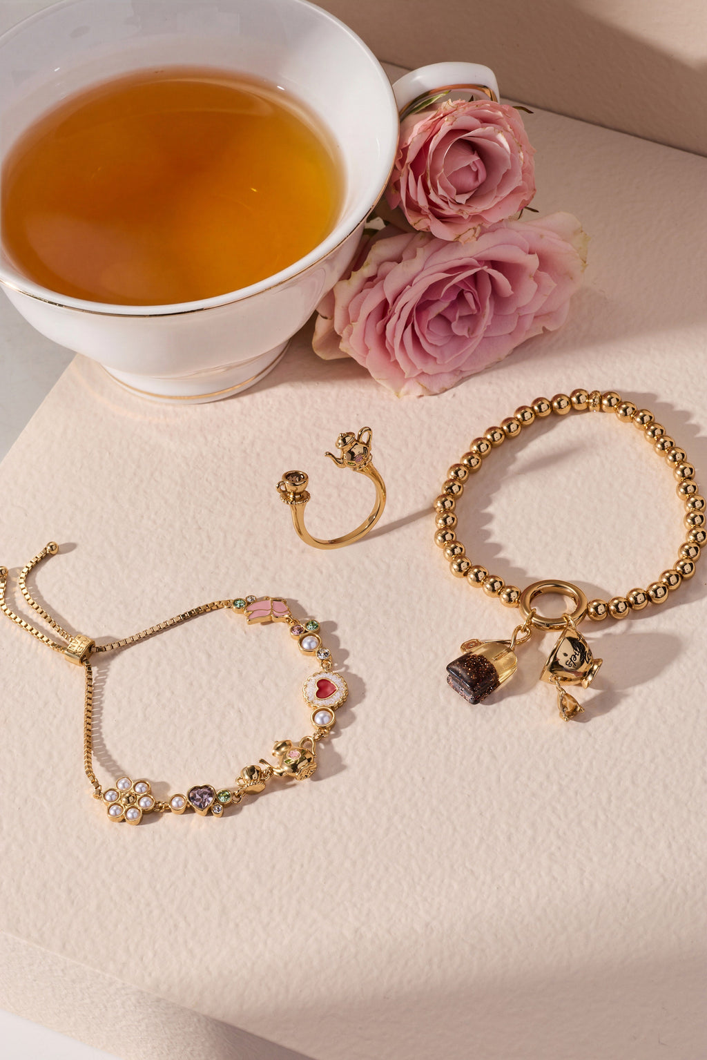 Gold-tone bolo bracelet with bow and tea-charm accents plus pearl bead details