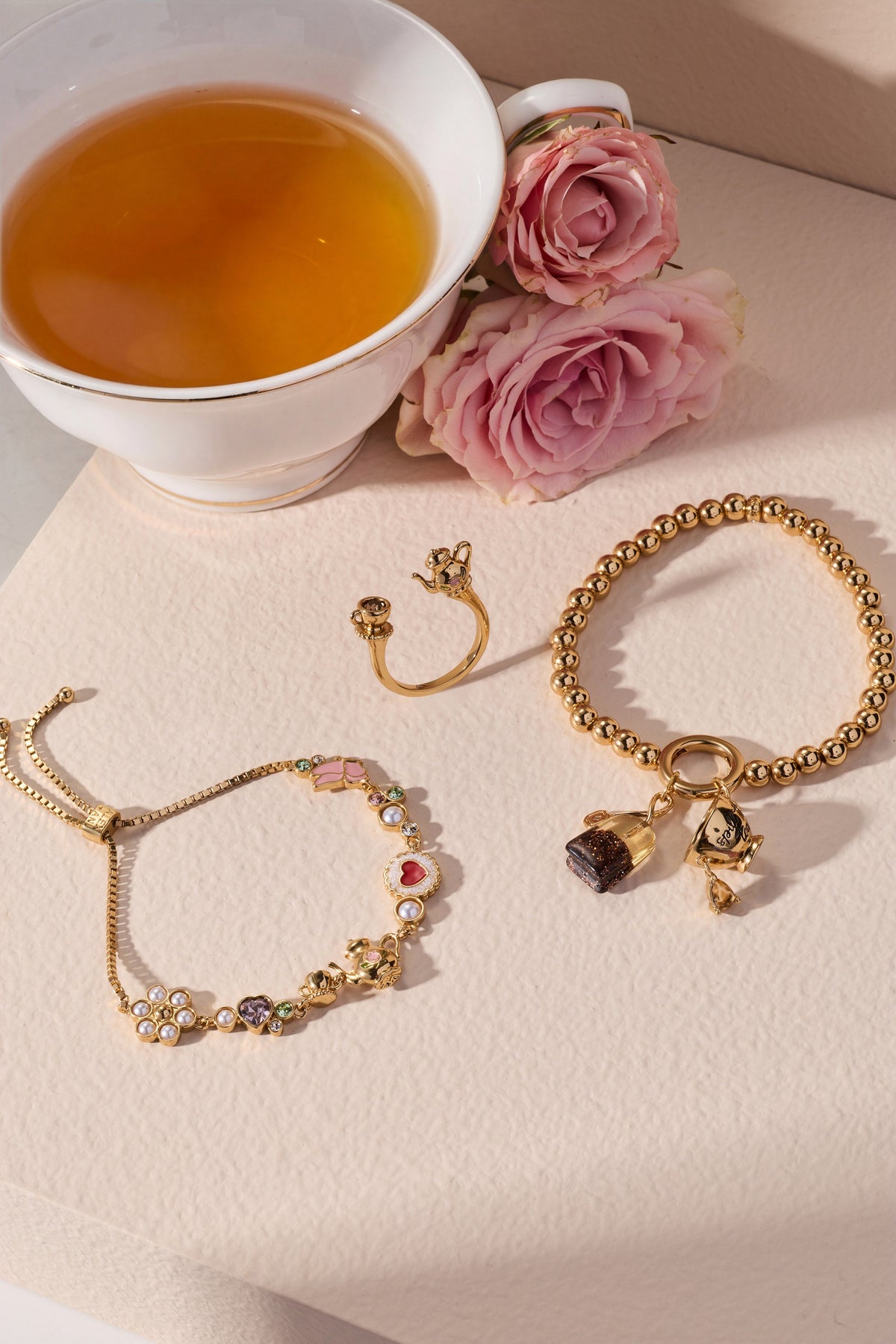 Gold-tone bolo bracelet with bow and tea-charm accents plus pearl bead details