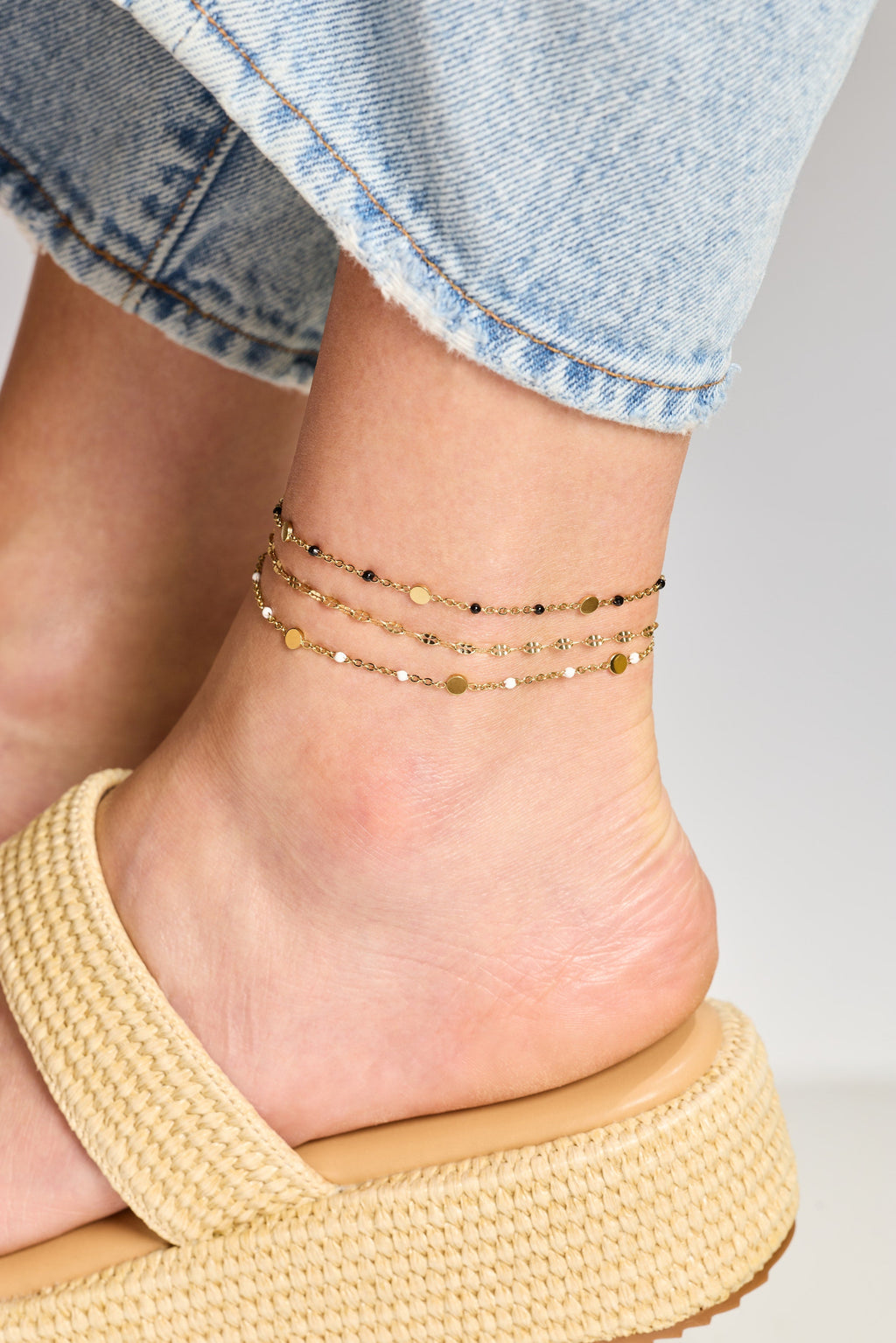 Gold chain anklet with tiny bead-like accents stacked on an ankle