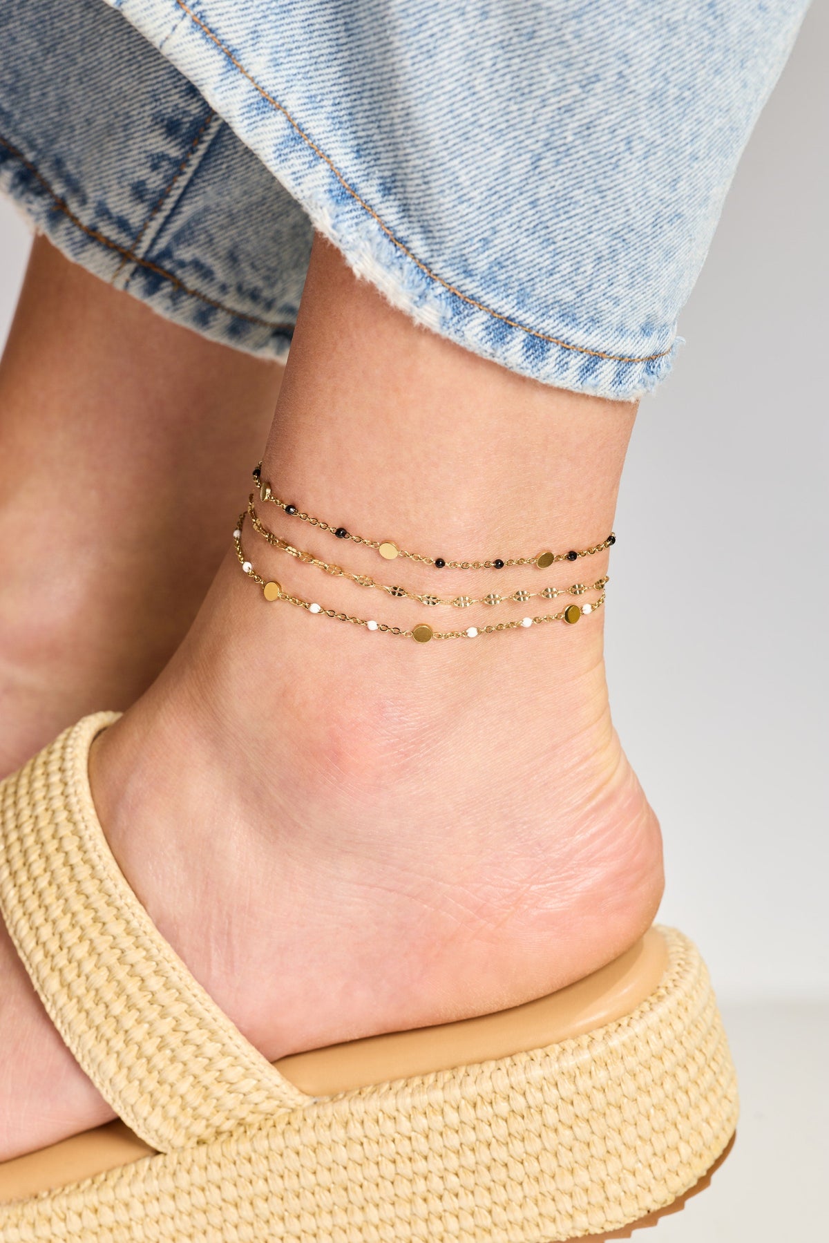 Gold chain anklet with tiny bead-like accents stacked on an ankle