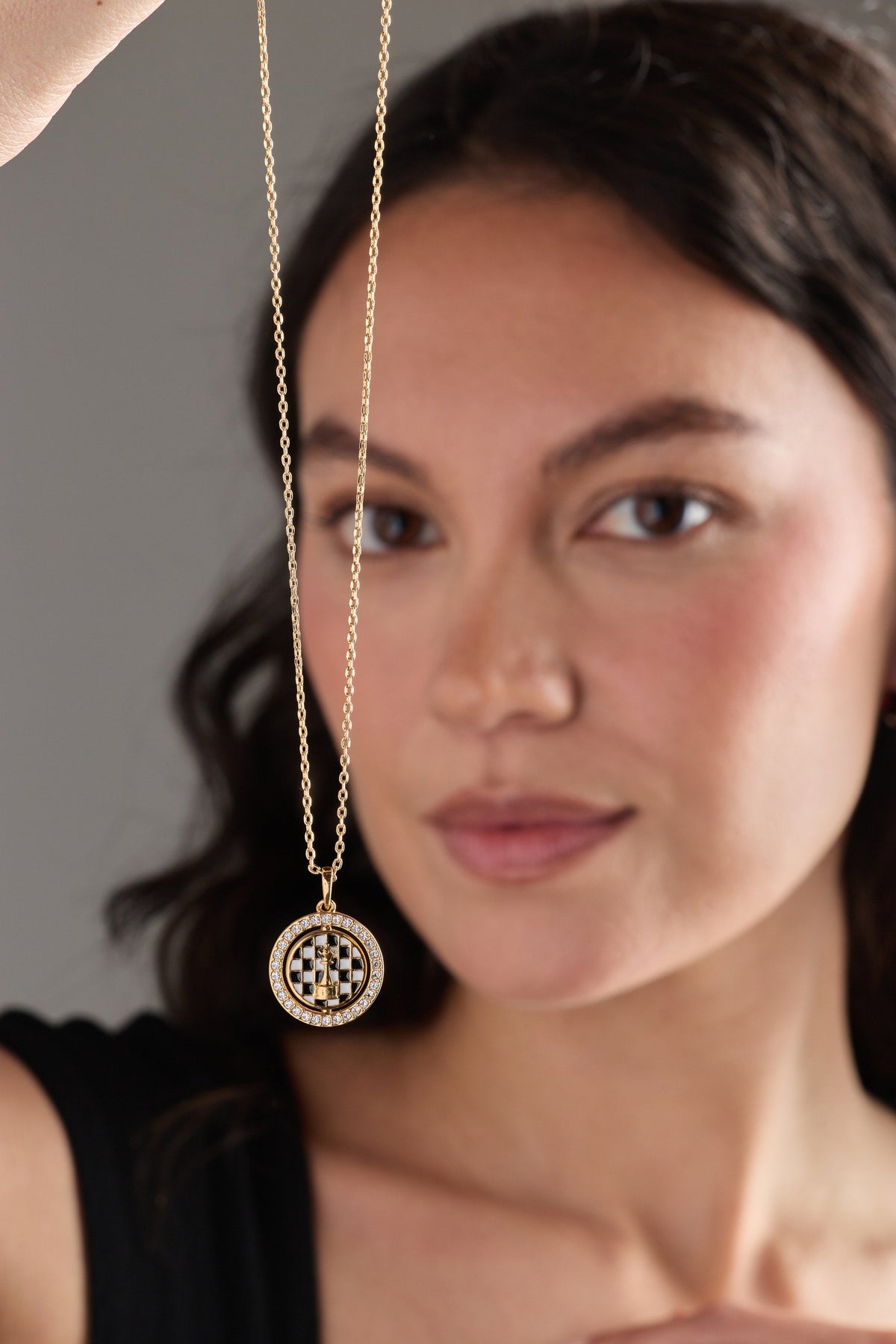 Gold chess spinner pendant necklace close-up with round crystal halo and checkered center