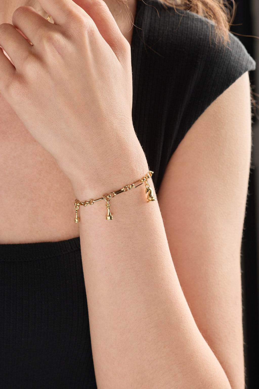 Gold chess charm bracelet on wrist with small hanging chess-piece charms