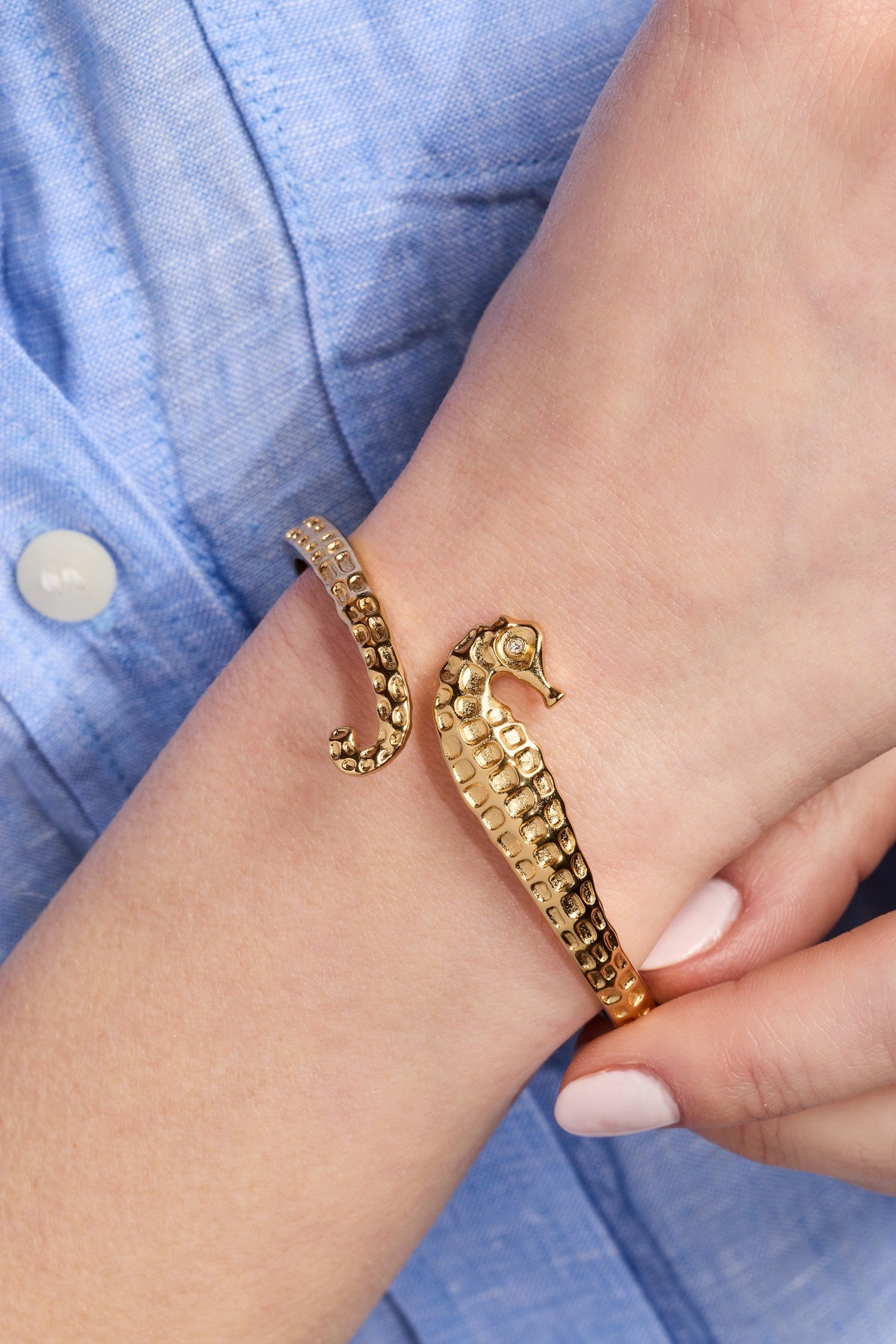 Gold-toned seahorse cuff bracelet on wrist with textured band and raised seahorse head