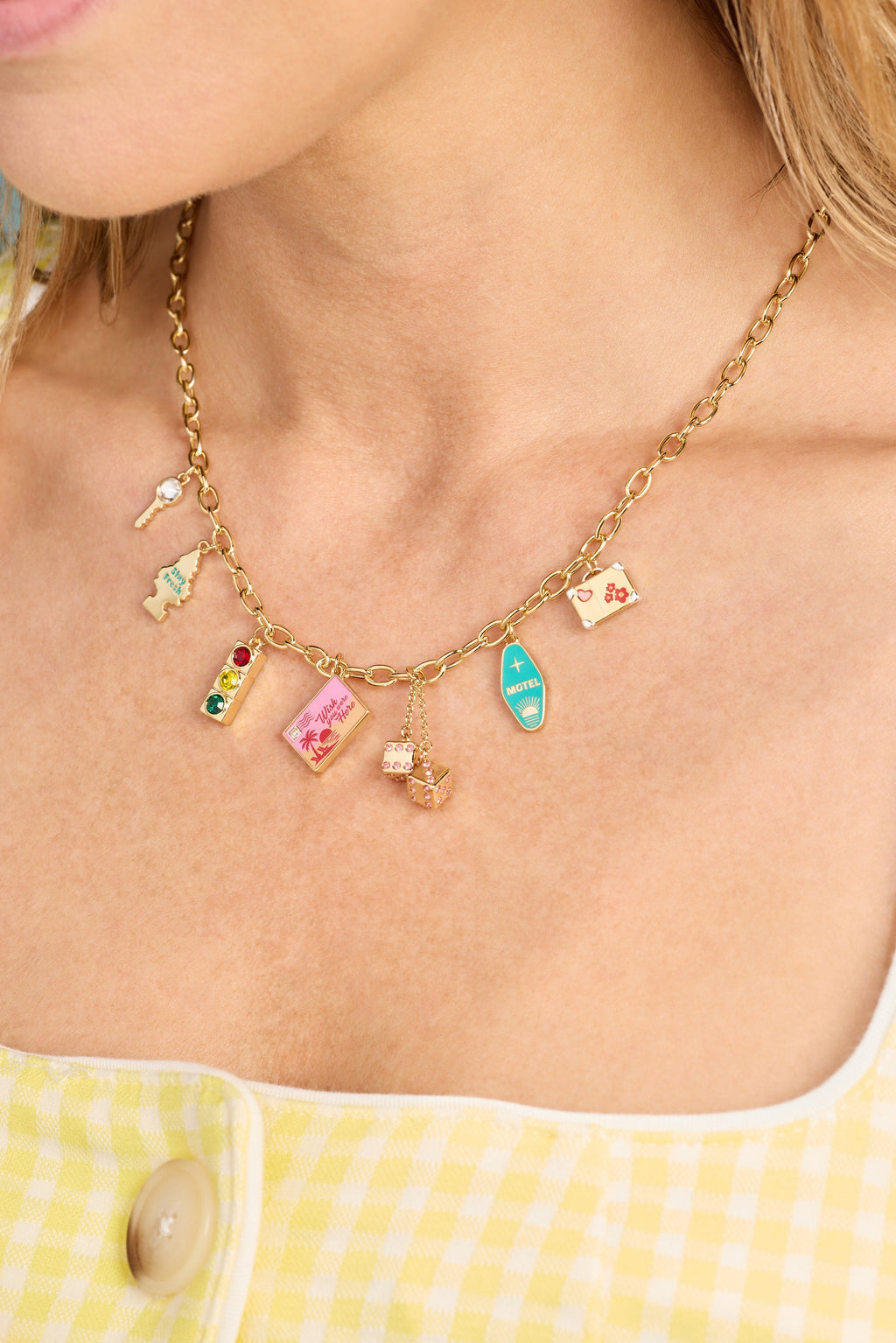 Gold multi-charm necklace with small travel pendants, worn close-up