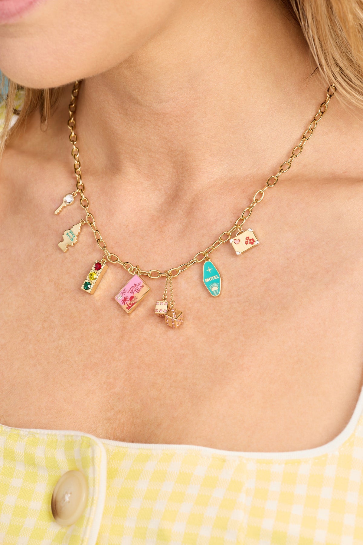 Gold multi-charm necklace with small travel pendants, worn close-up