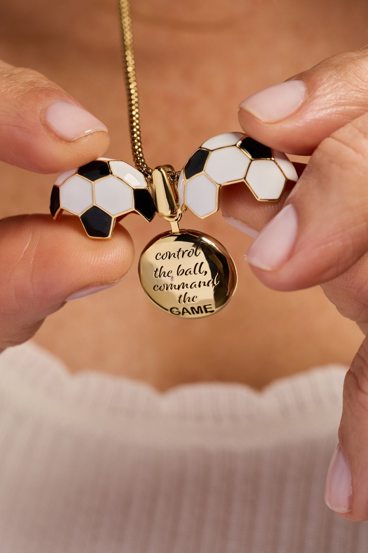 Gold soccer ball locket necklace with round locket text and soccer ball charms held by hands