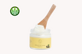 Shea body cream jar with white lid and pale yellow cream, scooped on wooden spoon