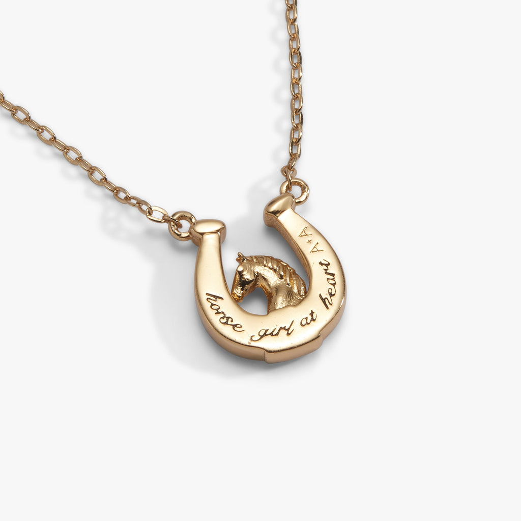Gold horseshoe pendant necklace with engraved wording along the charm, on chain